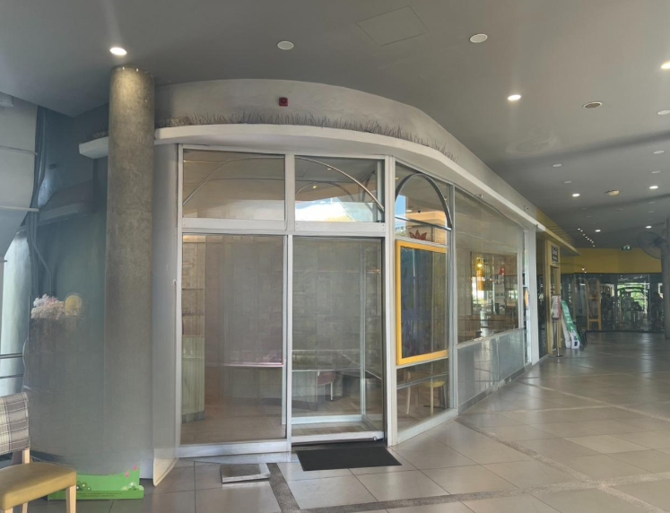 Retail Space for rent in Khlong Toei, Bangkok - Corner retail unit with floor-to-ceiling glass frontage, sliding doors, and a bright tiled mall corridor.