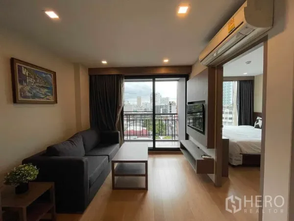 คอนโด ให้เช่าในWatthana, Bangkok - ห้องนั่งเล่นพร้อมโซฟาและผนังทีวี เปิดสู่ระเบียง เห็นวิวสกายไลน์ และทางเข้าห้องนอนแบบบานเลื่อน