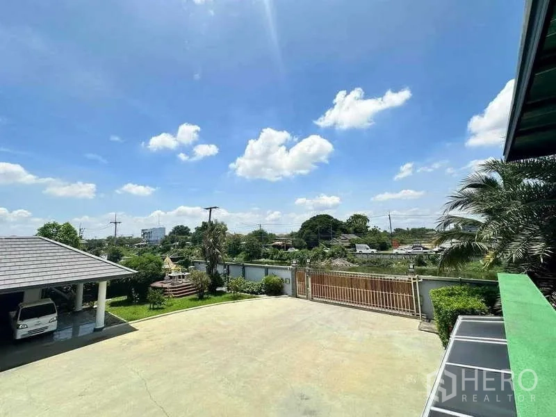 Detached House for sale in Khlong Luang, Pathum Thani - View over the driveway toward the sliding gate, canal and surrounding neighborhood.