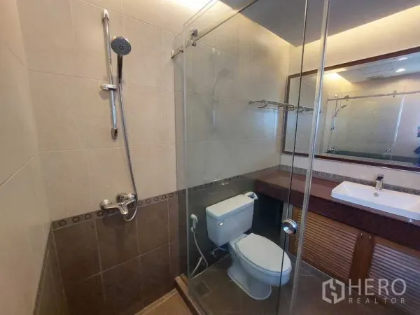 Apartment for rent - Modern bathroom featuring a glass-enclosed shower, toilet, large mirror and neutral wall tiles.