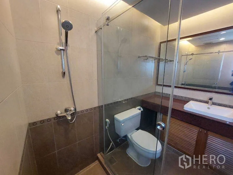 Apartment for rent - Modern bathroom featuring a glass-enclosed shower, toilet, large mirror and neutral wall tiles.