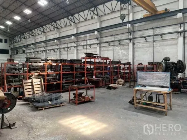 Factory for rent in Samut Prakan - High-ceiling production hall featuring red storage racks, industrial equipment and an overhead crane.