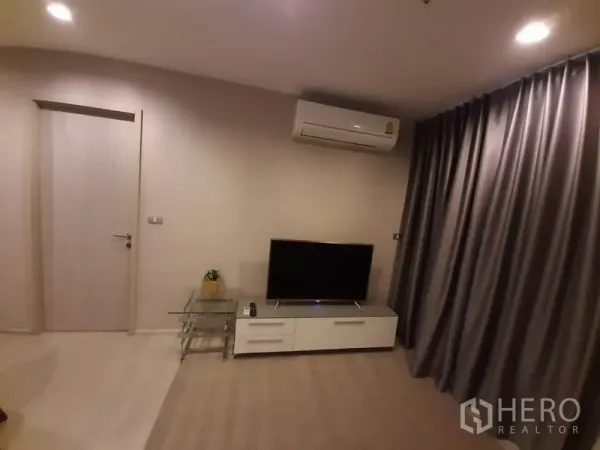 Condominium for rent or sale in Khlong Toei, Bangkok - TV unit and air conditioner facing full-length curtains in the living room.