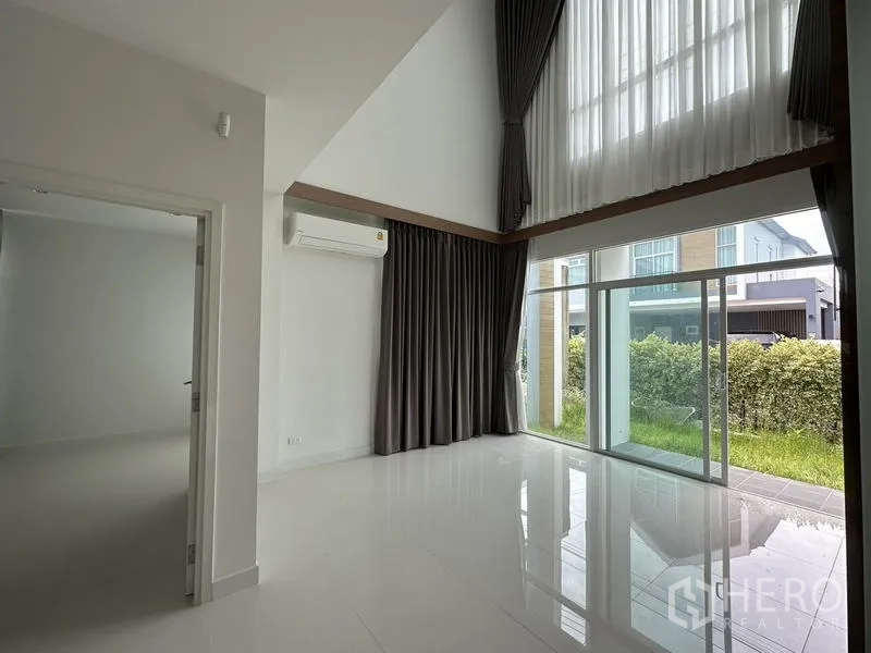 Detached House for sale in Lam Luk Ka, Pathum Thani - Bright living room with double-height ceiling and floor-to-ceiling windows with curtains.