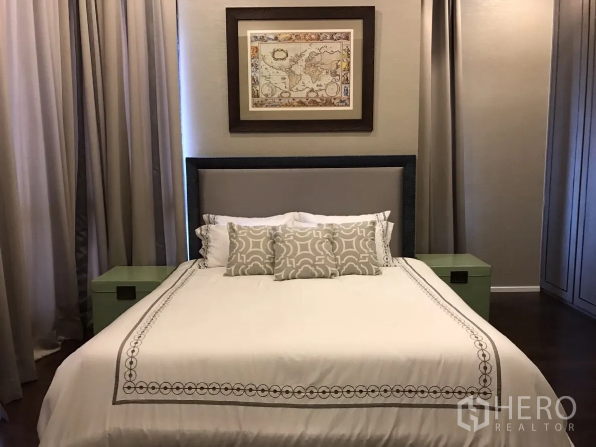 Condominium for rent or sale in Huai Khwang, Bangkok - Primary bedroom with upholstered headboard, neutral bedding, framed art and full-height curtains.