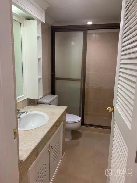 Condominium for sale in Watthana, Bangkok - Bathroom with stone-top vanity, toilet, and a glass-enclosed shower area.