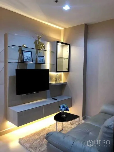 Condominium for rent or sale in Phaya Thai, Bangkok - Living room with wall-mounted TV, glass shelves and a sofa.