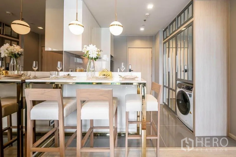 Condominium for rent or sale in Watthana, Bangkok - Dining island with pendant lights, bar stools and a built-in washer along the corridor.
