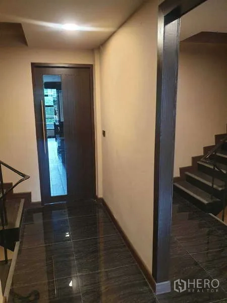 Home Office for rent in Khlong Toei, Bangkok - Hallway with glossy tiles leading to a staircase and a glass door.