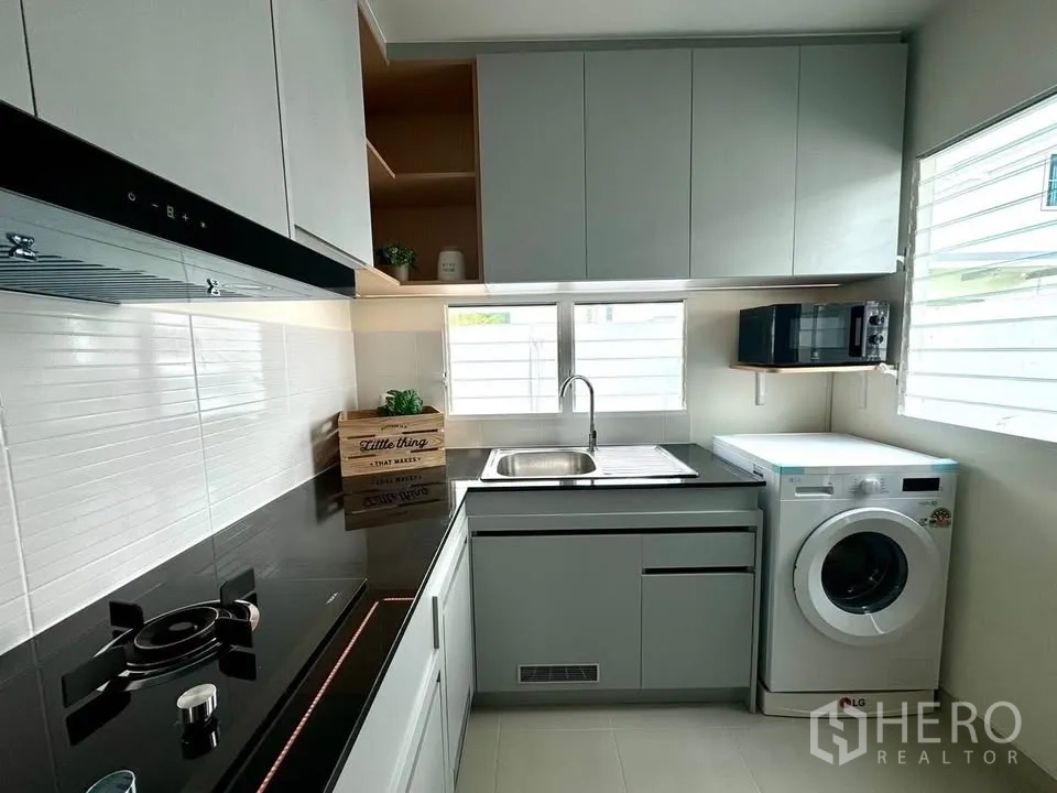 Detached House for rent in Bang Phli, Samut Prakan - Fitted kitchen with upper and lower cabinets, sink, cooktop, hood, and washing machine.