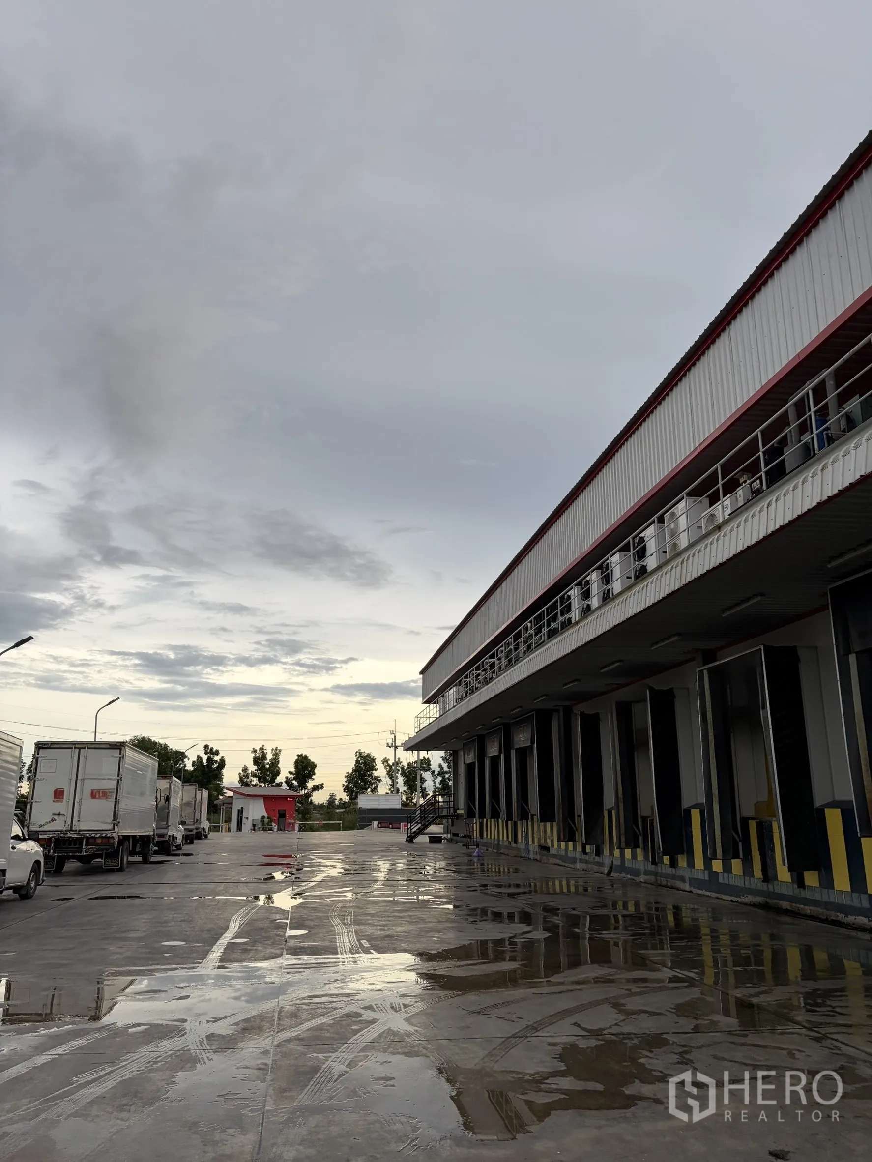 Factory for sale in Mueang Nakhon Pathom, Nakhon Pathom - Row of covered loading bays with trucks parked on a wide concrete apron.