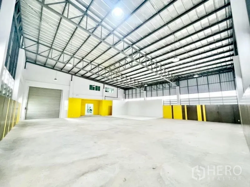 Warehouse for sale in Lam Luk Ka, Pathum Thani - Wide warehouse bay featuring a roller shutter and white cyclorama studio wall with ample floor space.