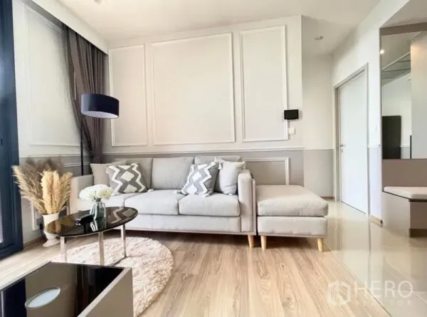 Condominium for rent in Khlong Toei, Bangkok - Contemporary lounge with L-shaped sofa, wall molding, wood floors and large window.