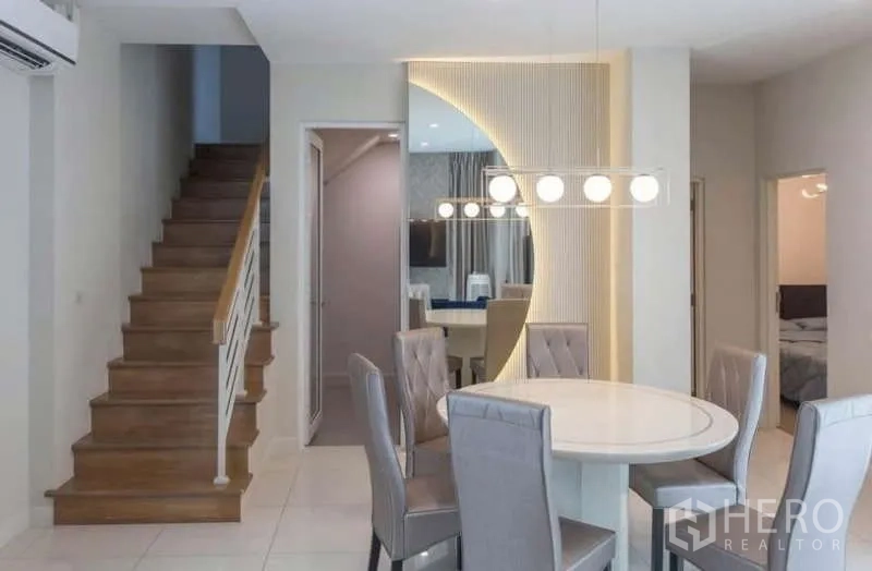 Detached House for rent or sale in Lat Phrao, Bangkok - Dining area with feature lighting beside a staircase and mirrored accent wall.