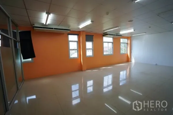 Factory for sale in Khlong Luang, Pathum Thani - Large office space with orange accent wall, windows and multiple air conditioners.