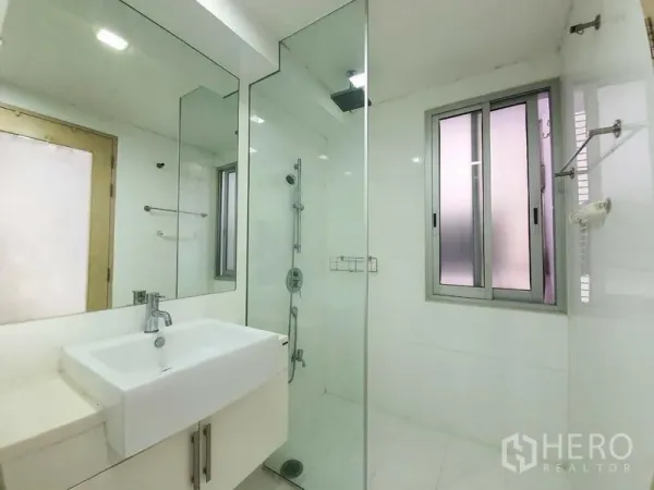 Condominium for rent in Din Daeng, Bangkok - Bright white bathroom with a glass-enclosed rain shower, large mirror, vanity sink, and window.