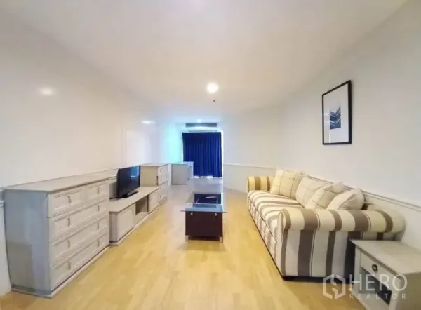 Condominium for rent in Khlong Toei, Bangkok - Long living area with sofa, TV cabinet, glass coffee table, and blackout curtains.