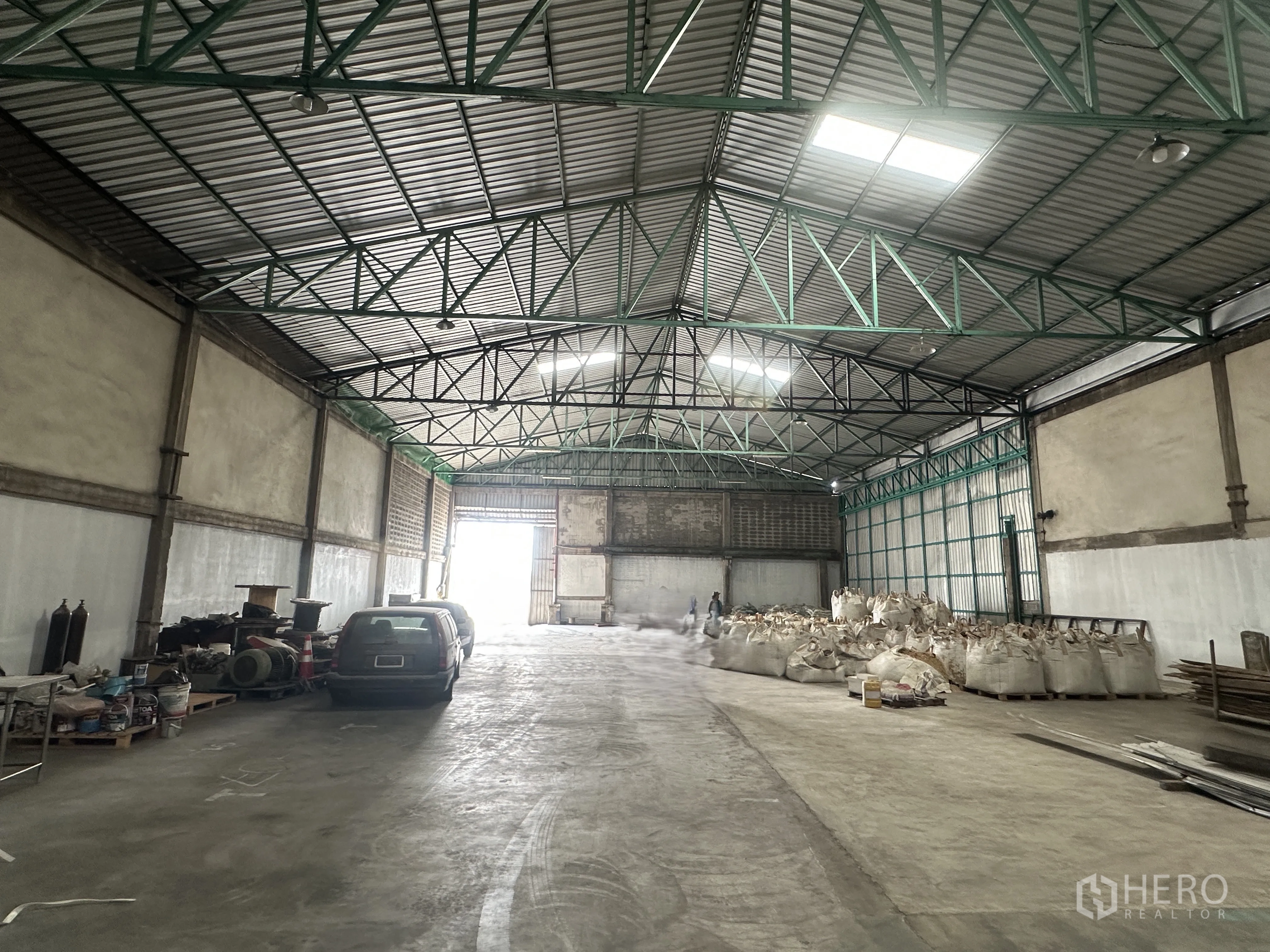 Warehouse for rent in Mueang Pathum Thani, Pathum Thani - Bright warehouse aisle facing a large sliding door with skylights and ventilated metal roof.