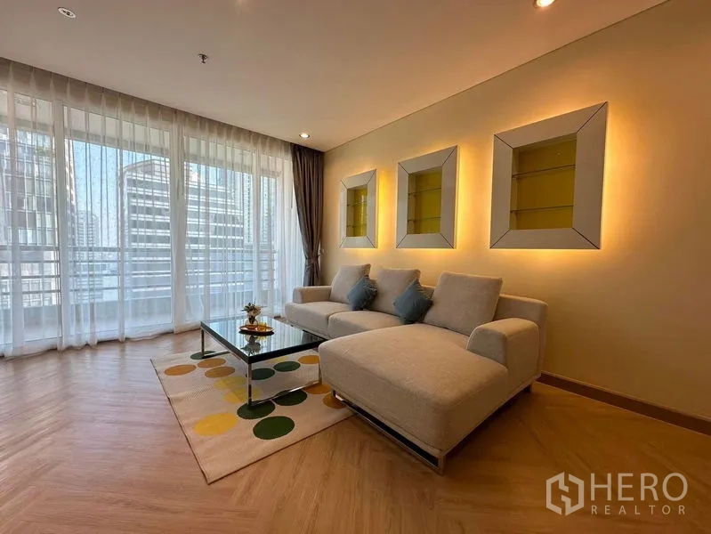 Condominium for rent in Bang Rak, Bangkok - Living area with sheer curtains, sectional sofa, and illuminated wall niches.