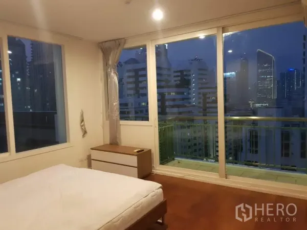 公寓 出租在Watthana, Bangkok - 主卧室设落地窗与阳台，木地板，可欣赏夜间城市天际线。
