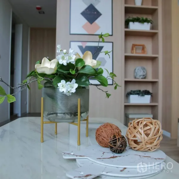 Condominium for rent or sale in Khlong Toei, Bangkok - Decorative vase and art on a marble table in a modern living space with built-in shelving.