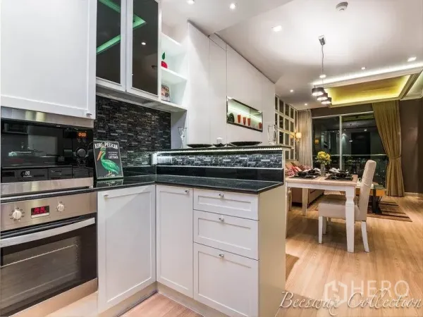 Condominium for rent in Watthana, Bangkok - Modern white U‑shaped kitchen with black granite counters, mosaic backsplash and built‑in oven facing the dining area.