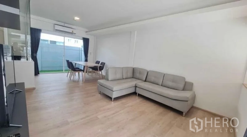 Townhouse for rent in Prawet, Bangkok - Open-plan living and dining area with an L-shaped sofa and sliding doors to the patio.
