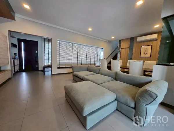 联排别墅 出租在Bang Phli, Samut Prakan - 宽敞客厅，转角沙发、落地百叶、筒灯和入户门一并可见。