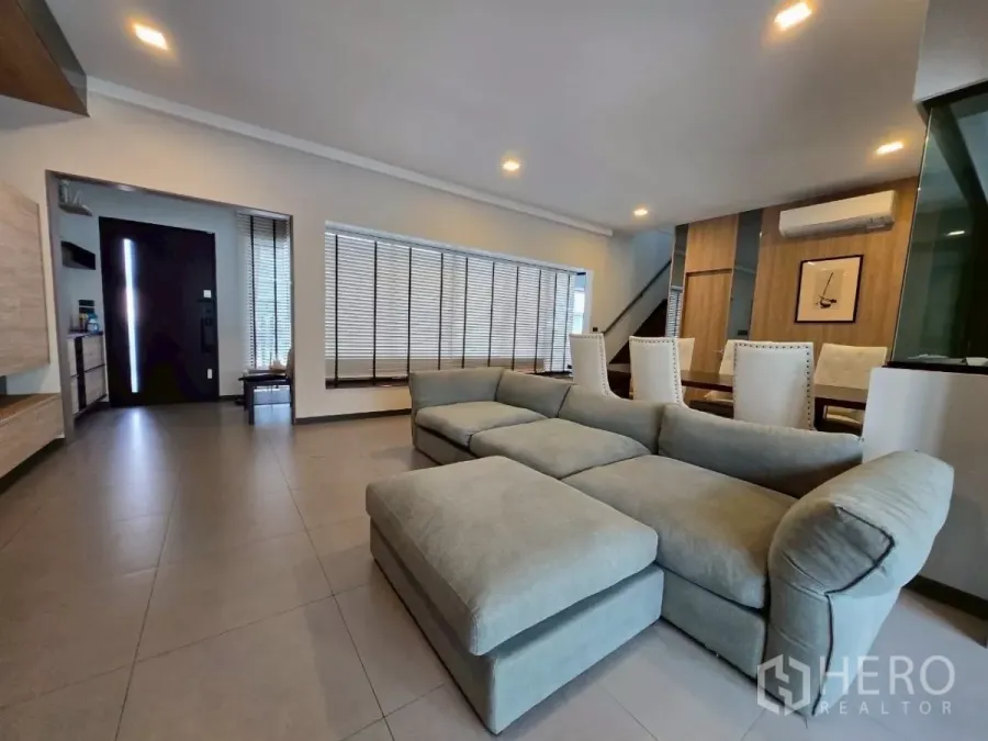 联排别墅 出租在Bang Phli, Samut Prakan - 宽敞客厅，转角沙发、落地百叶、筒灯和入户门一并可见。