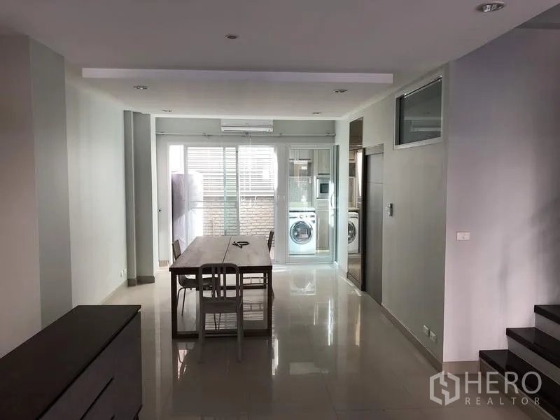 Townhouse for rent in Yan Nawa, Bangkok - Bright open-plan dining area with long table, glossy tile floors, sliding glass doors and a laundry nook.