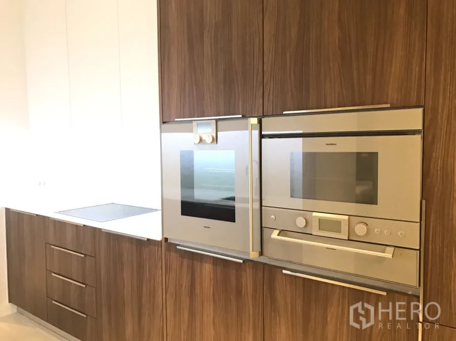 Condominium for rent in Pathum Wan, Bangkok - Modern kitchen with wood cabinetry, built-in oven, microwave and induction hob.