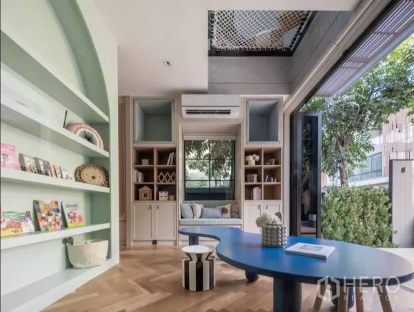 Detached House for rent or sale in Phra Khanong, Bangkok - Bright multipurpose room with mint built-in shelves, blue table, parquet flooring and garden view.