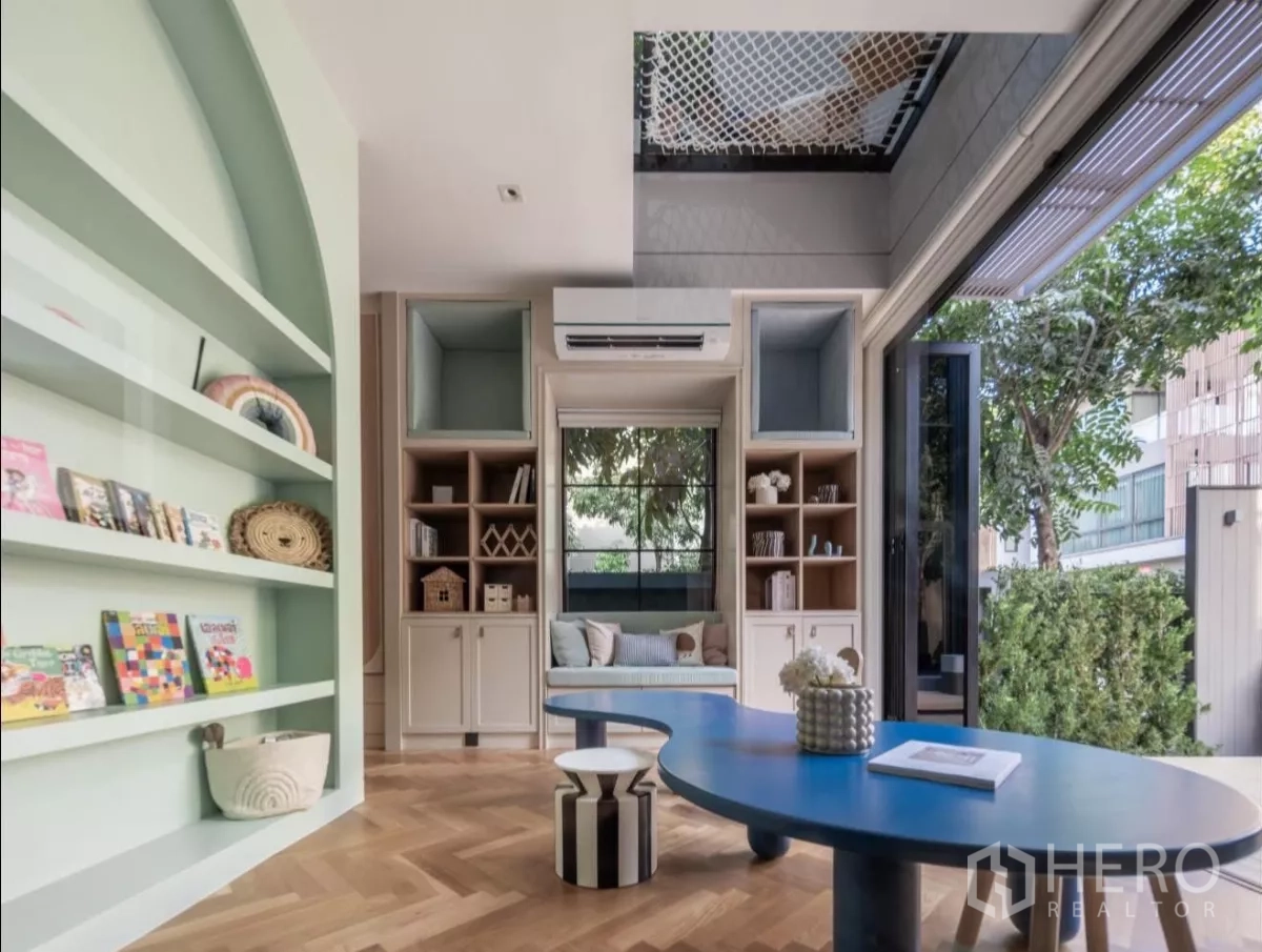 Detached House for rent or sale in Phra Khanong, Bangkok - Bright multipurpose room with mint built-in shelves, blue table, parquet flooring and garden view.