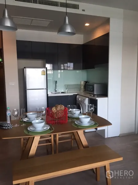 Condominium for rent or sale in Watthana, Bangkok - Dining table and bench beside a compact modern kitchen with glossy cabinets.