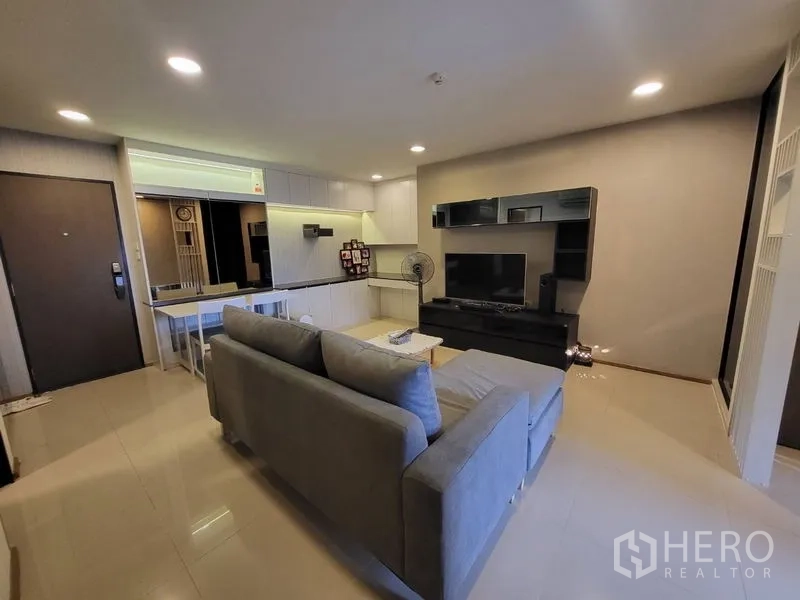 Condominium for rent or sale in Phaya Thai, Bangkok - Open-plan living room with grey sofa, TV unit and dining space.