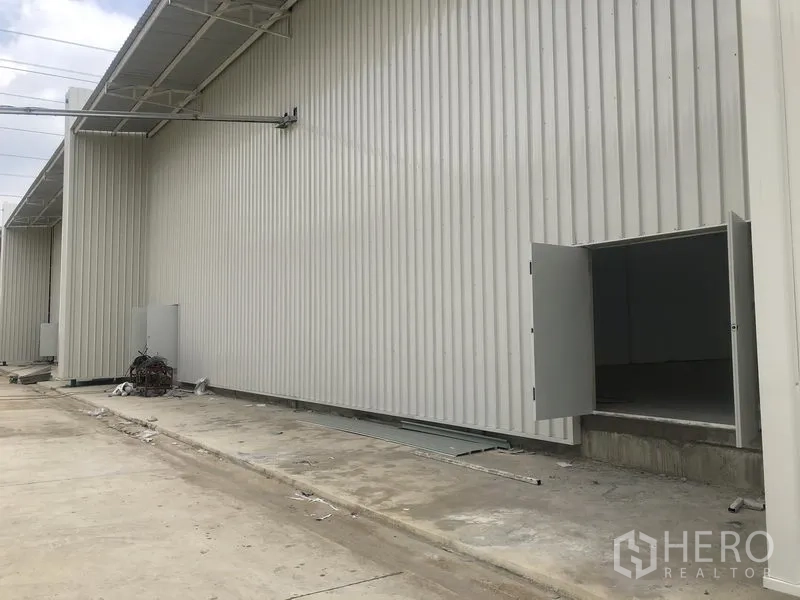 Factory for rent in Khlong Luang, Pathum Thani - Metal-clad warehouse side elevation with service doors open along the driveway.