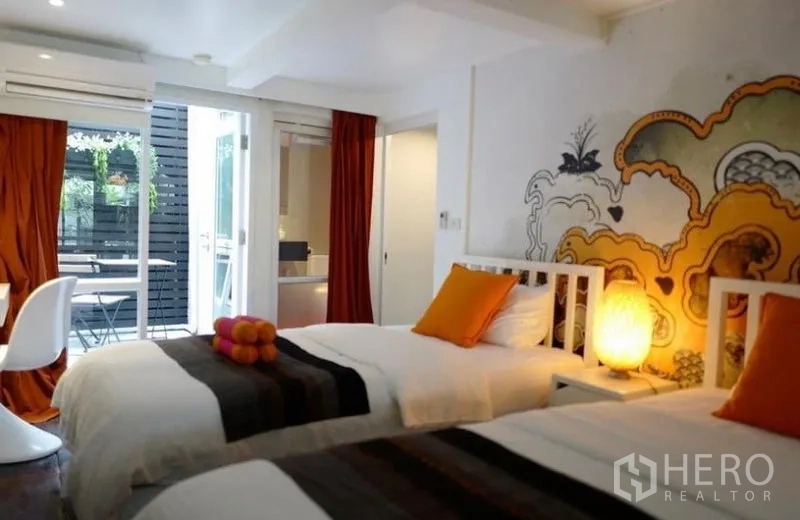 Townhouse for rent in Khlong Toei, Bangkok - Twin bedroom opening to a small terrace with mural wall and orange cushions.