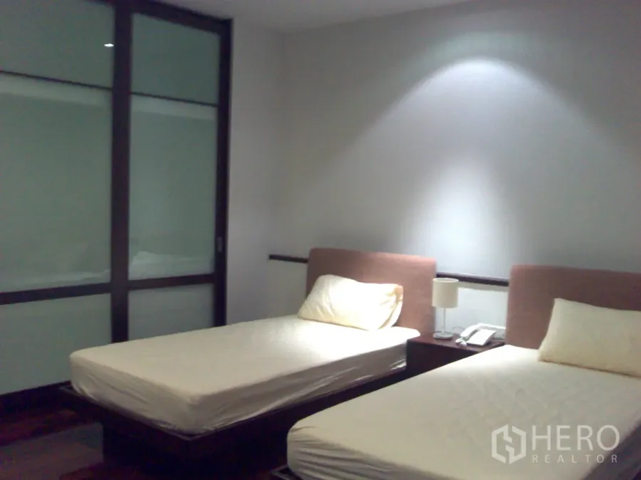 公寓 出租在Watthana, Bangkok - 双床卧室，柔和灯光，木地板与磨砂玻璃推拉衣柜门。