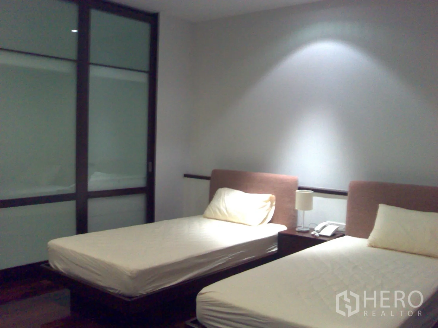 公寓 出租在Watthana, Bangkok - 双床卧室，柔和灯光，木地板与磨砂玻璃推拉衣柜门。