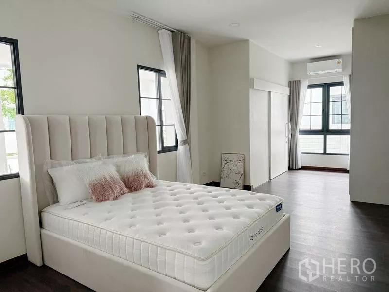 Detached House for rent or sale in Bang Phli, Samut Prakan - Additional bedroom with white bed, windows on two sides, wood floors and air conditioner.
