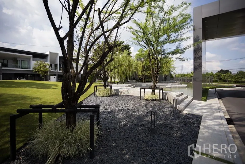 Townhouse for rent in Samut Prakan - Landscaped common garden with trees, gravel path and seating.