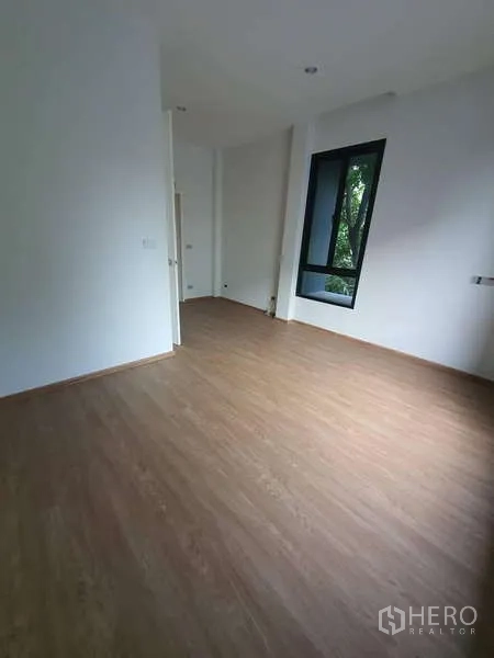 Detached House for rent in Phra Khanong, Bangkok - Spacious bedroom with wood floors and a tall corner window.