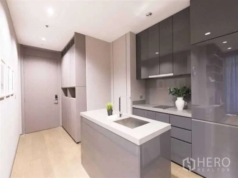 公寓 出租在Bang Rak, Bangkok - 走廊式厨房，亮光橱柜与岛台水槽，近入户门的整合电器。