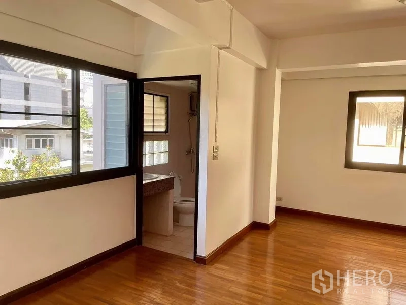 Home Office for rent in Khlong Toei, Bangkok - Sunlit bedroom with wood floor and ensuite bathroom visible through open door.