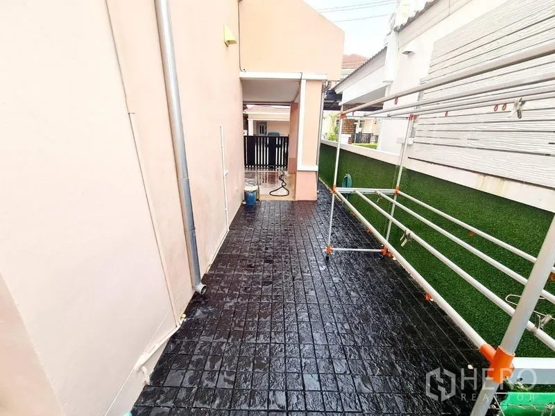 Detached House for rent in Sai Mai, Bangkok - Side yard with black tiled floor and metal drying racks under a roofed walkway.