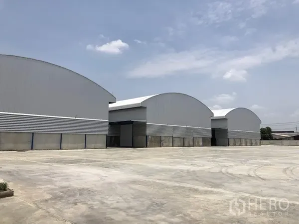 货栈 出租在Lat Lum Kaeo, Pathum Thani - 拱形屋顶的现代仓库外观，宽阔混凝土场地，晴朗天空。