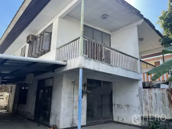独立式住宅 出售在Khlong Toei, Bangkok - 老式住宅近景，阳台略显斑驳，一层玻璃推门与金属屋顶车棚。
