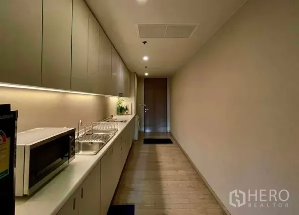 公寓 出租在Watthana, Bangkok - 长廊式厨房，整排橱柜、洗槽和微波炉，搭配灯带照明。