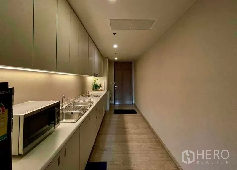 公寓 出租在Watthana, Bangkok - 长廊式厨房，整排橱柜、洗槽和微波炉，搭配灯带照明。