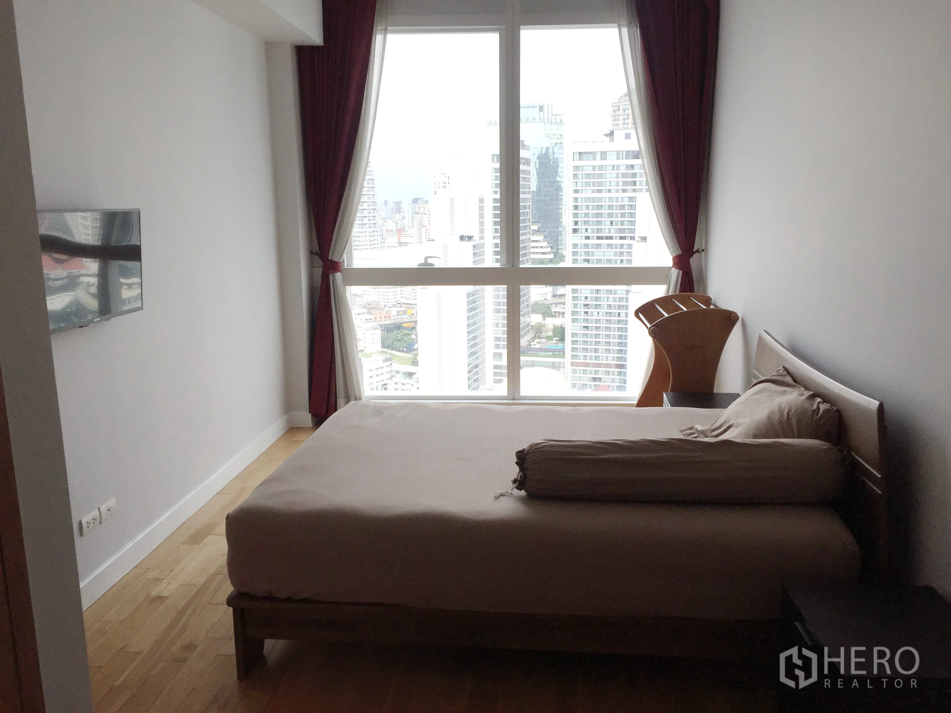Condominium for rent in Khlong Toei, Bangkok - Second bedroom with large window, city skyline view and wall-mounted TV.